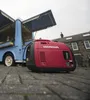 A red Honda generator is placed on a paved surface in front of a blue food truck with its serving windows open. Buildings are visible in the background. Produktbild-Vorschau
