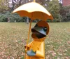 A garden statue of a frog wearing a yellow raincoat and holding an umbrella. Produktbild-Vorschau
