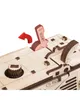 Close-up view of a wooden model of a self-propelled mower, focusing on the control panel with levers and a dial. A red arrow indicates a lever's movement. Podgląd zdjęcia produktu