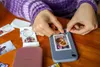 A person is decorating a phone case with small printed photos. Podgląd zdjęcia produktu