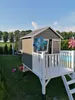 A wooden playhouse in a backyard setting with a trampoline and a sandbox. Produktbild-Vorschau
