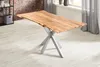 A wooden dining table with a live edge top and a silver spider leg base, placed on a light-colored floor in a room with a brick wall and curtains. Produktbild-Vorschau