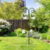 A garden scene with a black metal shepherd's hook holding two white planters with white flowers. Produktbild-Vorschau