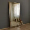 A full-length mirror with a decorative frame leans against a gray wall. Dried flowers in vases are placed in front of the mirror on a wooden floor. Produktbild-Vorschau