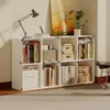 A white bookshelf filled with books and decorative boxes, placed in a room with a painting and a plant. Podgląd zdjęcia produktu