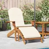 A wooden Adirondack chair with a cream cushion and footrest is placed on a patio next to a small wooden table with drinks. Podgląd zdjęcia produktu