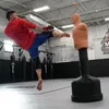 A man is practicing martial arts by kicking a dummy in a gym. Podgląd zdjęcia produktu