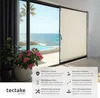 A retractable awning is shown partially deployed in front of a sliding glass door overlooking a tropical pool and ocean view. Plants are in the foreground. Náhled obrázku produktu