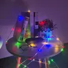 A table with books, glasses, and a string of colorful LED lights. Produktbild-Vorschau