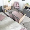 A nursery room with a crib attached to a bed, a chair, and a dresser. Produktbild-Vorschau