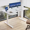 A white L-shaped standing desk with dual monitors, a keyboard, a mouse, a tablet, and a book. Anteprima dell’immagine prodotto