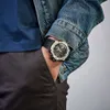A person's hand with a watch is in their pocket, wearing a denim jacket. Produktbild-Vorschau