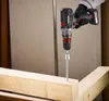 A person is using a cordless drill to screw a long screw into a wooden beam. Podgląd zdjęcia produktu