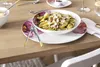 A table setting with a bowl of pasta on a decorative plate, with cutlery and a glass of water. Voir les images du produit