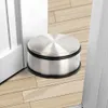 A stainless steel door stopper with a black rubber base sits on a light wood floor next to a white door. Voir les images du produit