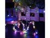Two heart-shaped string lights with multicolor LEDs are displayed in the foreground, with a blurred background of decorative plants and a white fence. Podgląd zdjęcia produktu