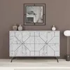 A white marble sideboard with a geometric pattern is displayed against a brown wall. A mirror hangs above the sideboard, and two decorative vases are placed on top. A floor lamp is visible to the right. Náhled obrázku produktu