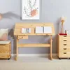 A wooden children's desk with adjustable height and tilt, placed in a room with a grey wall and a storage chest next to it. Produktbild-Vorschau