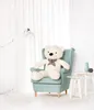 A large white teddy bear sits in a light blue armchair in a brightly lit room with white curtains. Podgląd zdjęcia produktu