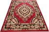 A red and beige patterned rug is shown from a diagonal angle on a white background. Náhled obrázku produktu