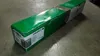 A green and white cardboard box for a Lexmark toner cartridge, lying on a concrete floor. Voir les images du produit