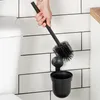 A hand holding a black toilet brush over a black holder mounted on a tiled wall next to a toilet. Anteprima dell’immagine prodotto