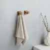 Two copper bathroom hooks mounted on a light gray wall, with a beige towel hanging from one hook. A white vase with branches is on the right. Anteprima dell’immagine prodotto