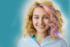 A young woman with blonde curly hair is smiling at the camera. Her hair has colorful streaks of purple and orange, and some strands are braided with small green beads. She is wearing a light blue collared shirt. There are faint, light-colored heart shapes  Produktbild-Vorschau