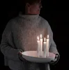 A person holding a white ceramic candle holder with four white candles lit in it. Produktbild-Vorschau