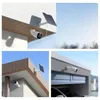 Collage of three images showing a white wireless security camera with a solar panel mounted on different exterior surfaces of a building. Produktbild-Vorschau