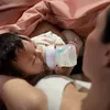 A baby is being fed from a bottle by a person. Podgląd zdjęcia produktu