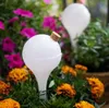 Two white watering globes with cork stoppers are placed in a garden bed with colorful flowers. Anteprima dell’immagine prodotto