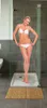 A woman in a bikini is standing in a shower stall, with water spraying on her. Produktbild-Vorschau