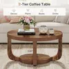 A round, two-tier coffee table with a rustic wood finish, placed in a living room setting with a sofa in the background. Anteprima dell’immagine prodotto