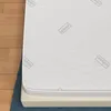A mattress with a silver cover is shown on a blue mat, with a wooden floor in the background. Produktbild-Vorschau