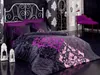 A luxurious bedroom setting with a bed dressed in a patterned duvet cover, pillows, and a bolster. Decorative lanterns and a purple accent chair are also visible. Podgląd zdjęcia produktu