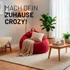A cozy living room scene with a red beanbag chair, a blanket, a plant, and a coffee table. Voir les images du produit