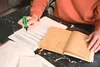 A person is highlighting text on a document with a green highlighter, with an open notebook next to it. Anteprima dell’immagine prodotto