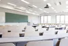 An empty classroom with rows of desks and chairs, a projector on the ceiling, and a green chalkboard on the wall. Produktbild-Vorschau