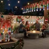 People celebrating Christmas outdoors at night with string lights and a fire pit. Náhled obrázku produktu