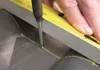 A hand is using a screwdriver to mark a line on a dark surface, guided by a yellow level. Anteprima dell’immagine prodotto