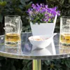 Two beer mugs and a bowl of nuts on a round metal table with a potted plant. Voir les images du produit