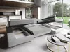 A modern living room with a large sectional sofa that has been partially converted into a bed, showcasing its storage and sleeping features. The room has large windows overlooking a garden. Produktbild-Vorschau