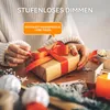 A person is wrapping a gift with an orange ribbon, surrounded by festive decorations and a lit candle. Produktbild-Vorschau