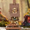 A miniature wooden windmill house with a water wheel, set in a whimsical, mossy forest background with a hobbit-like dwelling in the distance. Náhľad obrázku produktu