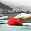A hand holding a red silicone phone holder on a car dashboard with a scenic view in the background. Voir les images du produit