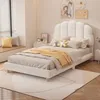 A bedroom scene with a white upholstered bed as the main focus, decorated with pillows and a throw blanket. The room has a window with blinds and decorative wall art. Produktbild-Vorschau