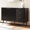 A black sideboard with gold accents and fluted detailing, standing on tapered legs with gold tips. A white vase with branches is placed on top. Voir les images du produit