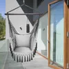 A gray hanging chair with tassels and a pillow is shown on a balcony next to a glass door. Produktbild-Vorschau