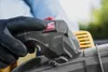 A gloved hand pressing a red button on a leaf blower. Produktbild-Vorschau